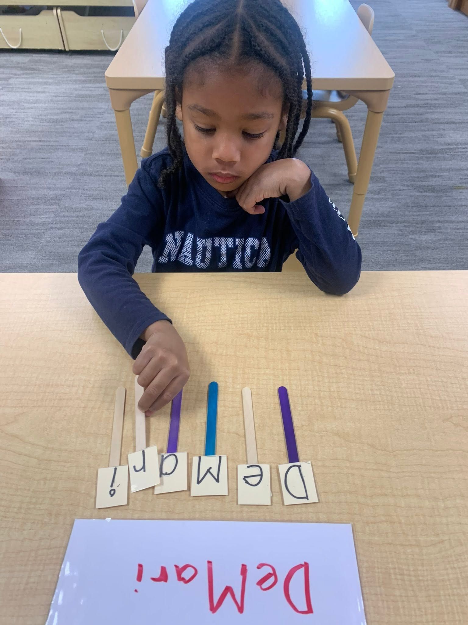 Child arranges letter cards beside a red “Demonstration” word on a classroom table.