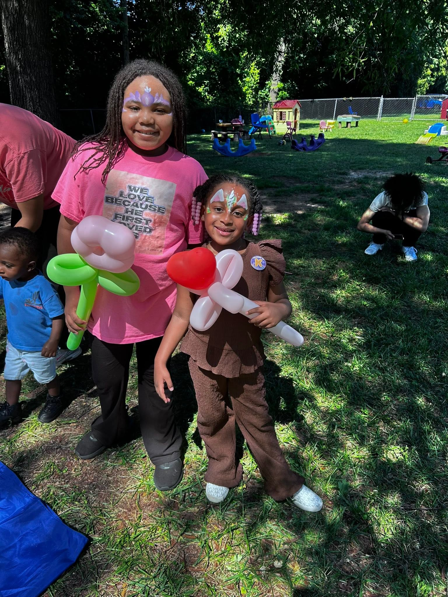 Two children holding balloon animals at a sunny outdoor party in a grassy park