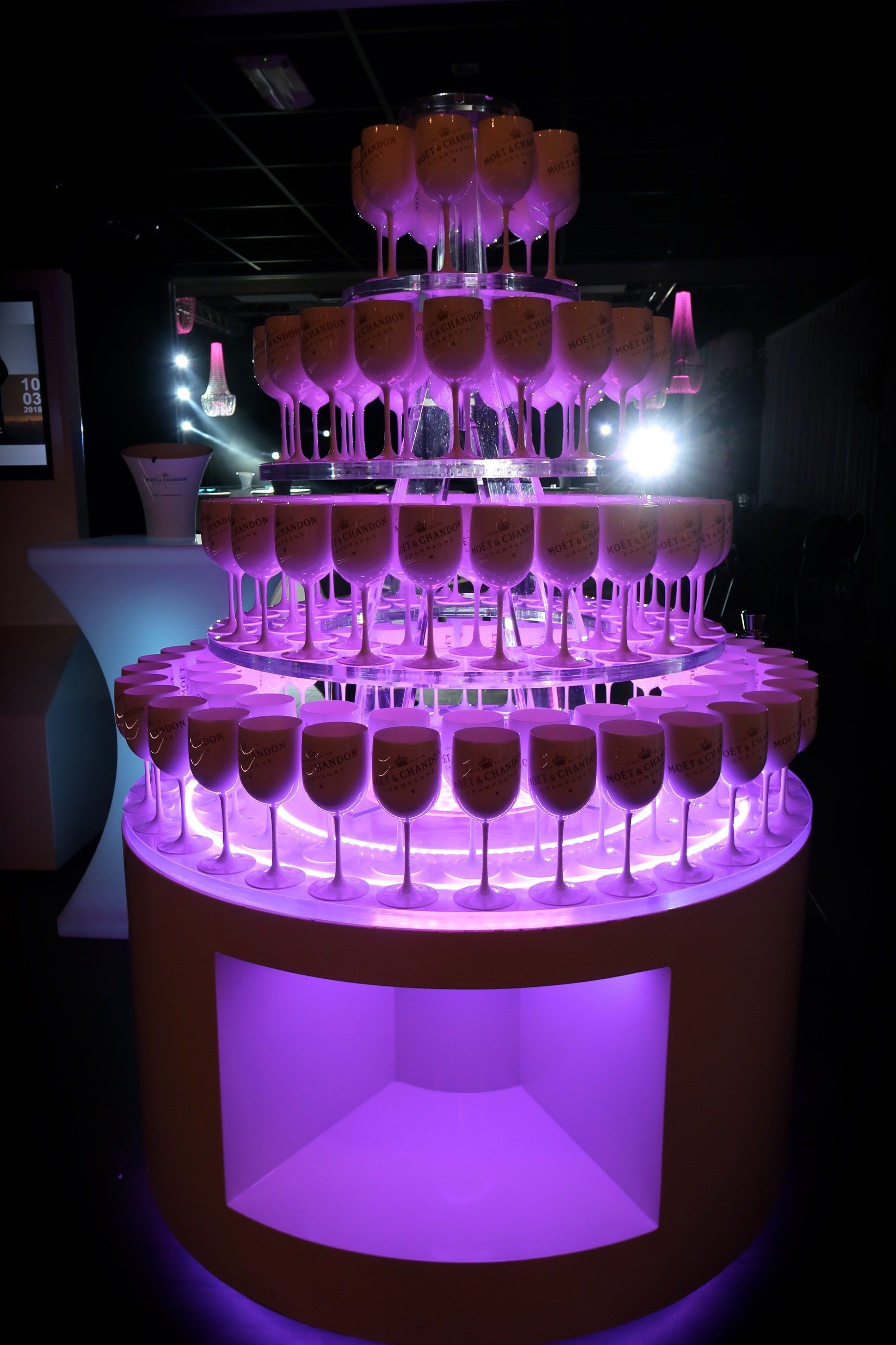 Champagnetoren met verlichte paarse voet en niveaus, gevulde glazen, evenementsetting.