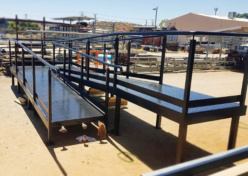 A metal ramp with a railing is sitting on top of a dirt field.