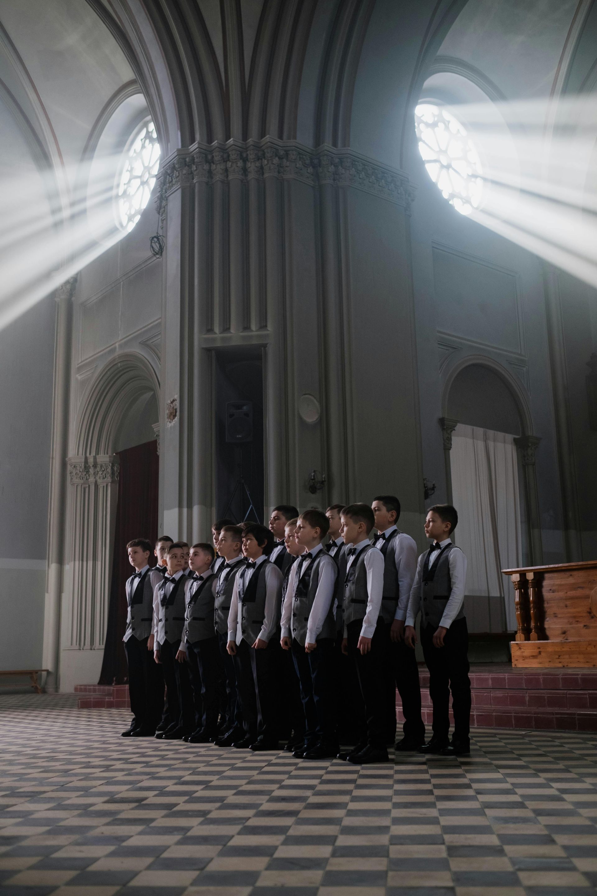 Choir in formal attire singing in a church with sunlight beams.