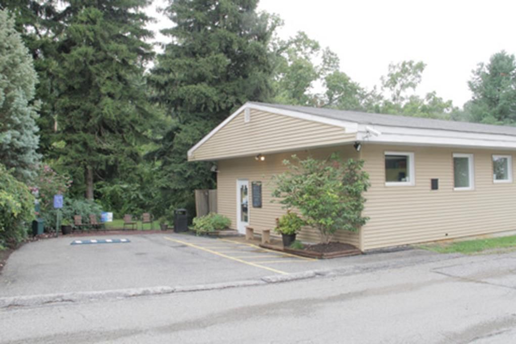 Tan building with parking area and trees.