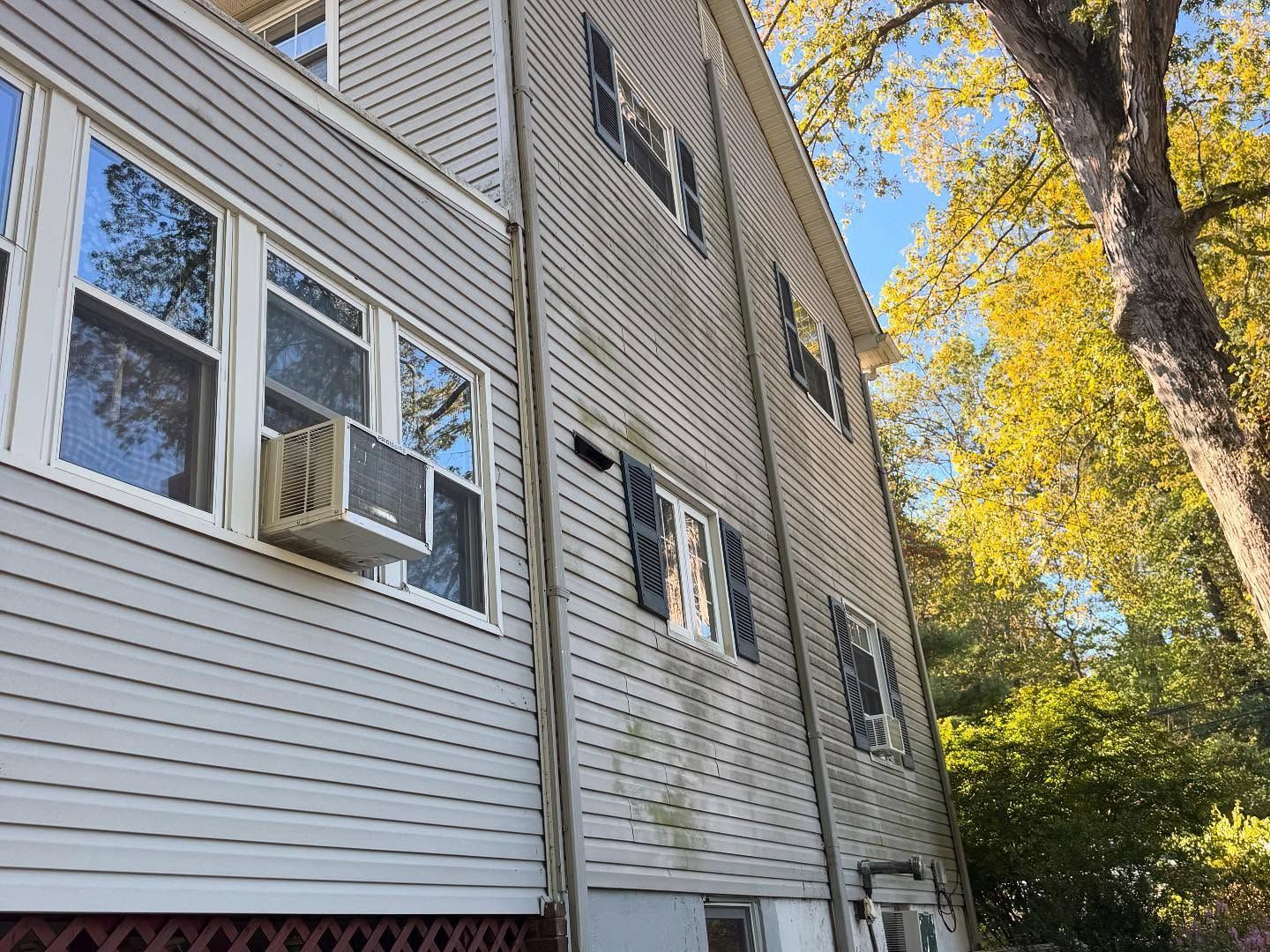 Apartment building exterior with beige siding, windows, and an air conditioner beside autumn trees