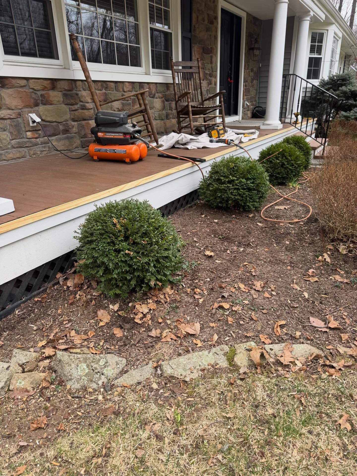 Front porch with tools and debris during repairs, including an orange lawnmower and potted shrubs.