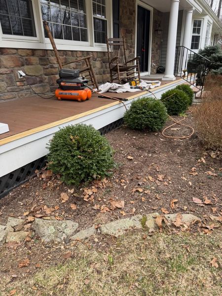 Front porch with tools and debris during repairs, including an orange lawnmower and potted shrubs.