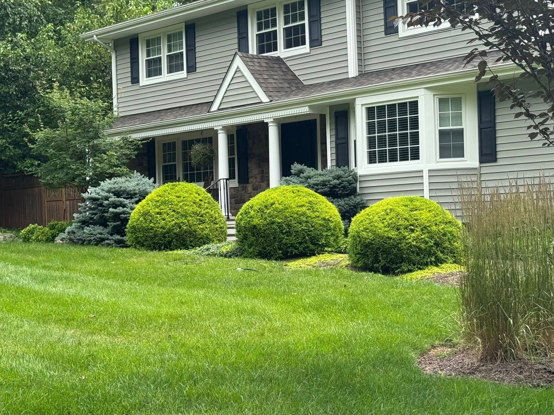 Two-story gray house with white trim, front porch, and manicured green lawn and shrubs