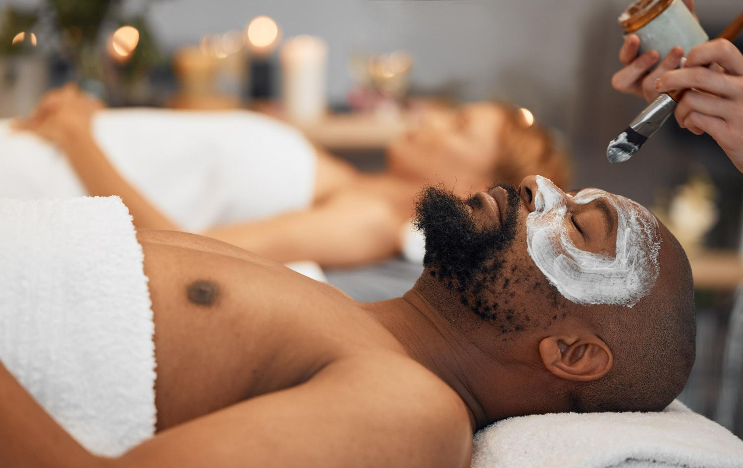 A person receiving a facial treatment with a white mask applied to their skin in a relaxing spa setting.