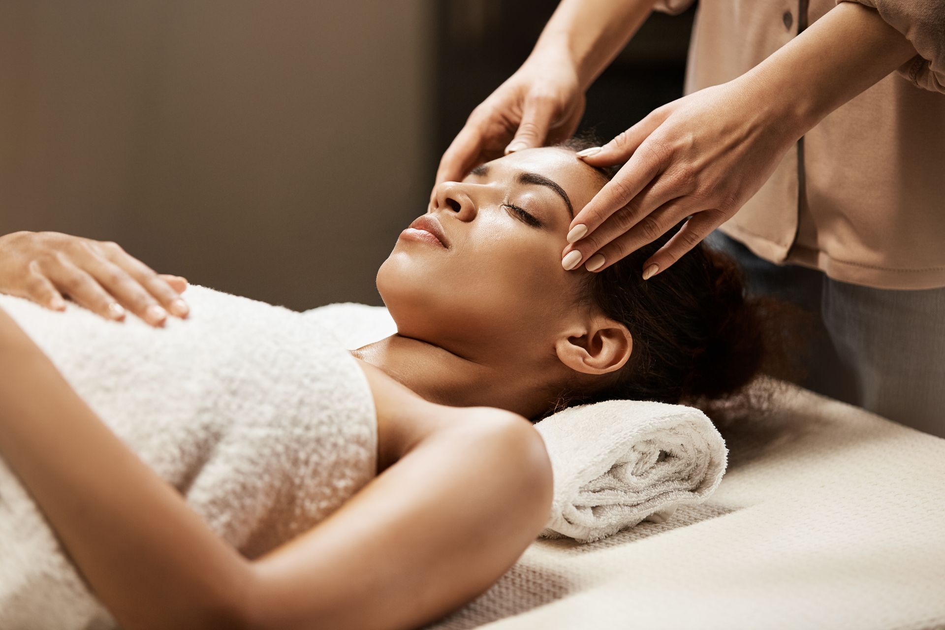 Facial spa treatment with hands massaging a woman’s forehead in a warm, serene setting