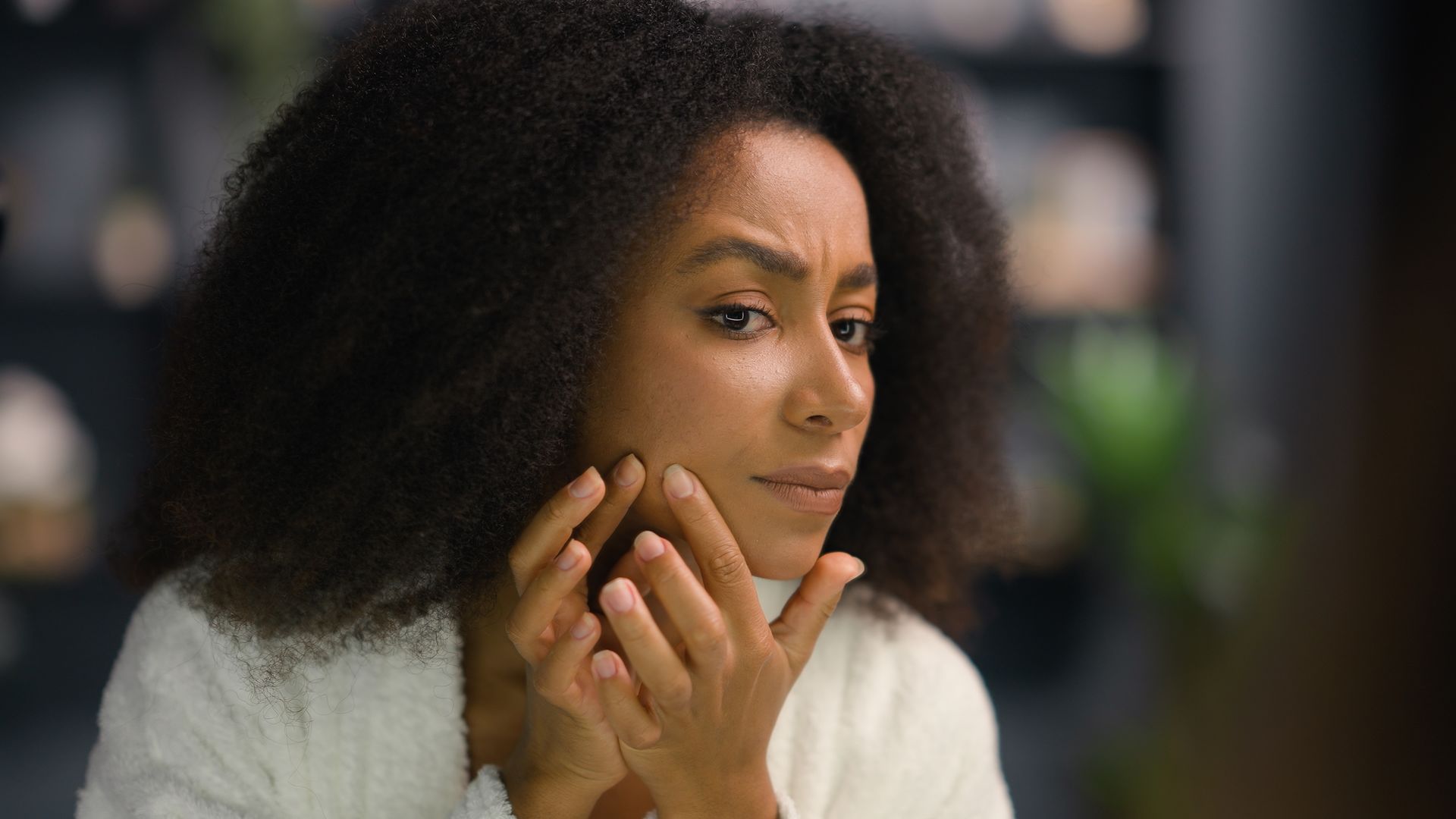 Woman resting chin on hands, looking thoughtfully to the side in a softly blurred indoor setting.