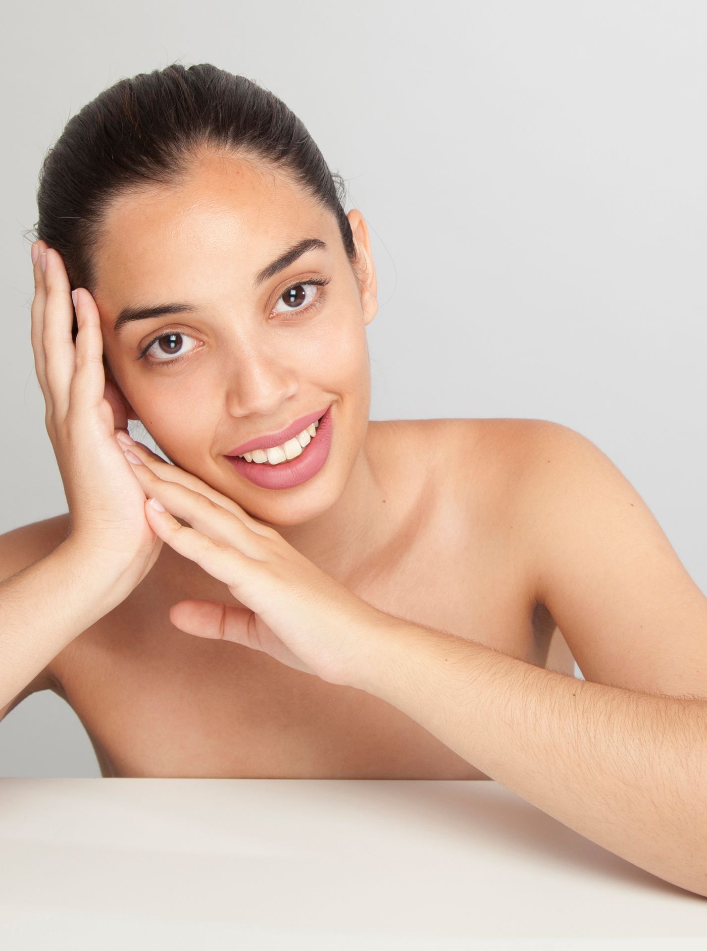 A woman is touching her face with her hands and smiling.