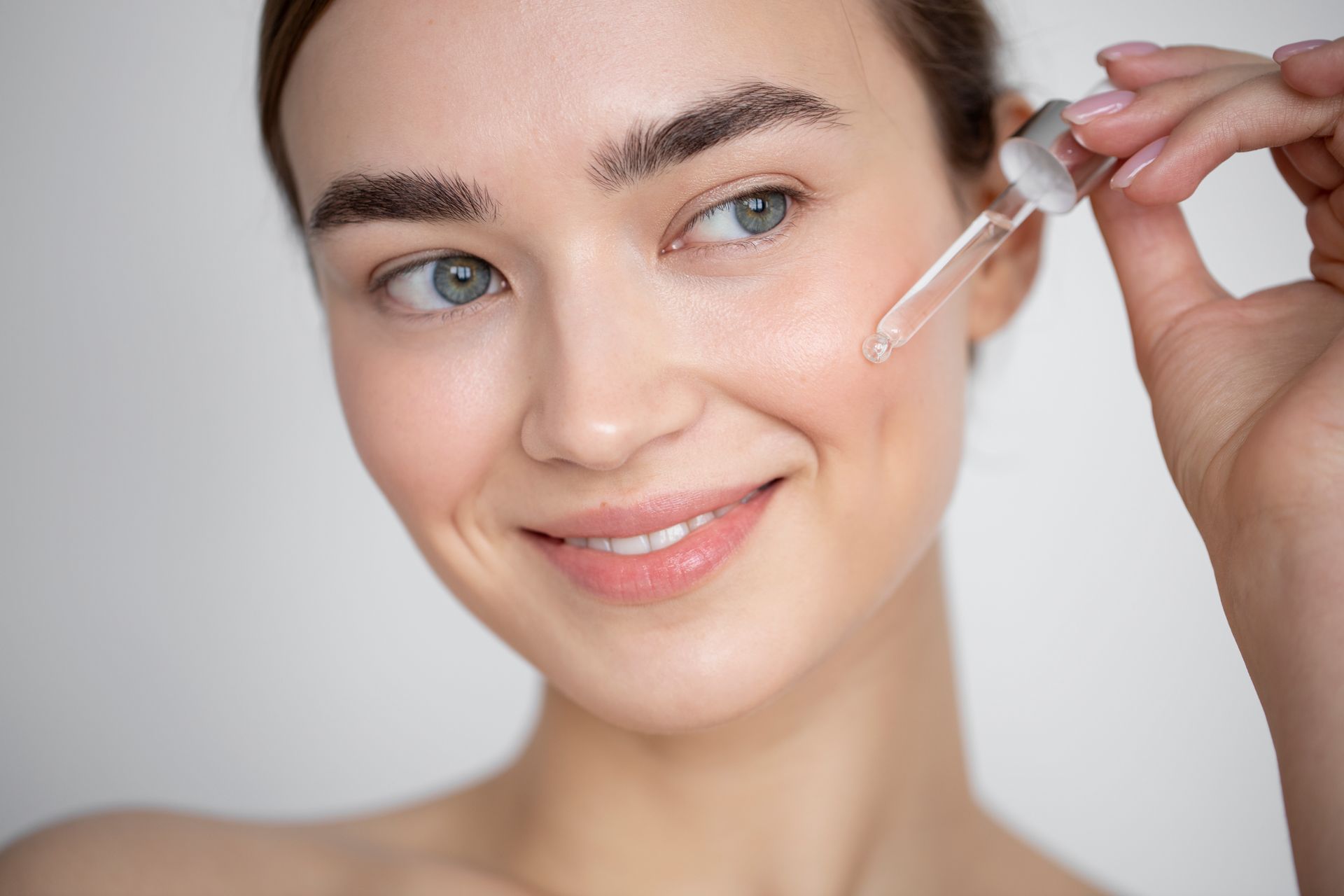 Smiling person applying facial serum with a dropper near the cheek