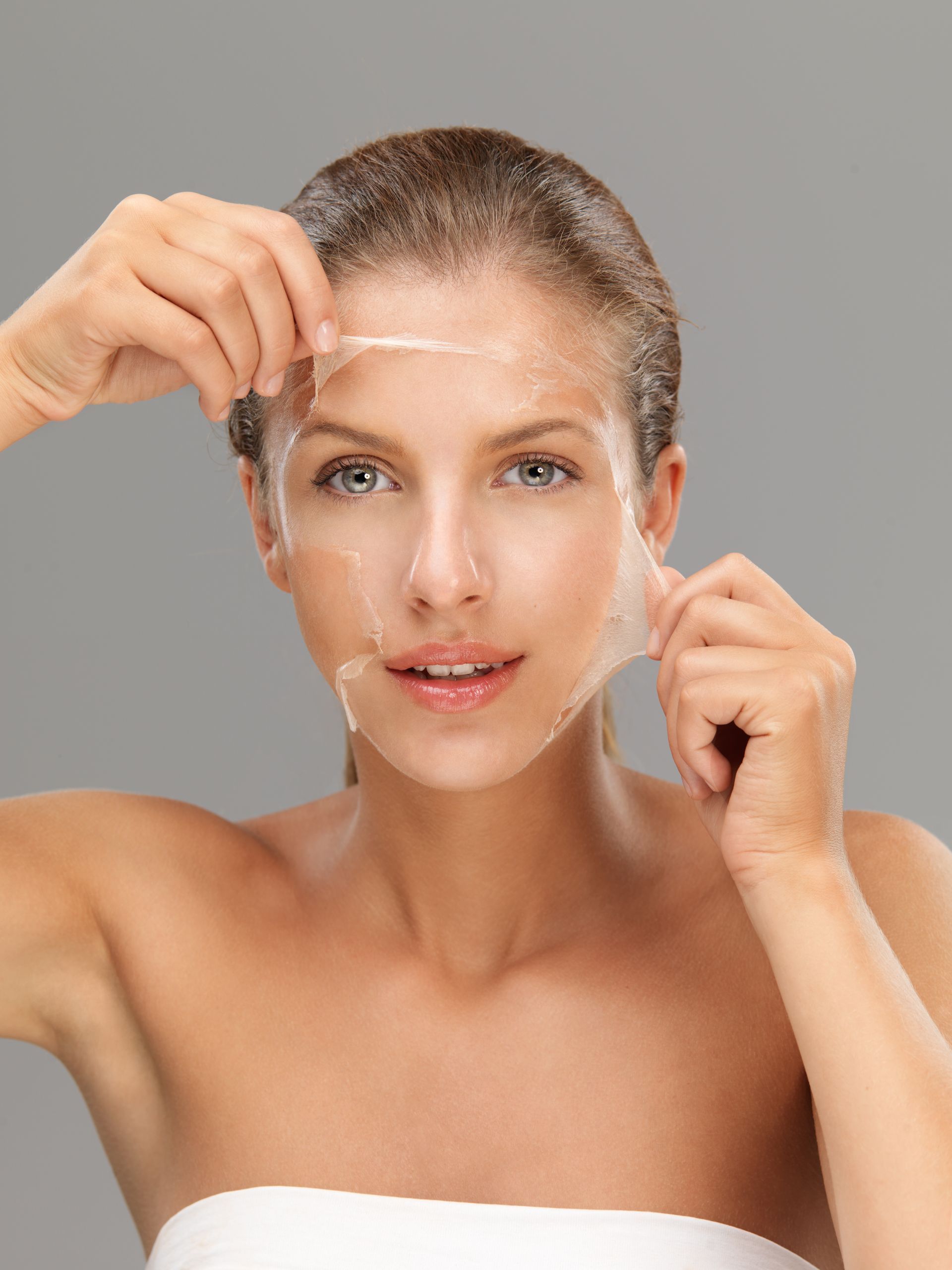 A woman is peeling off a mask from her face.