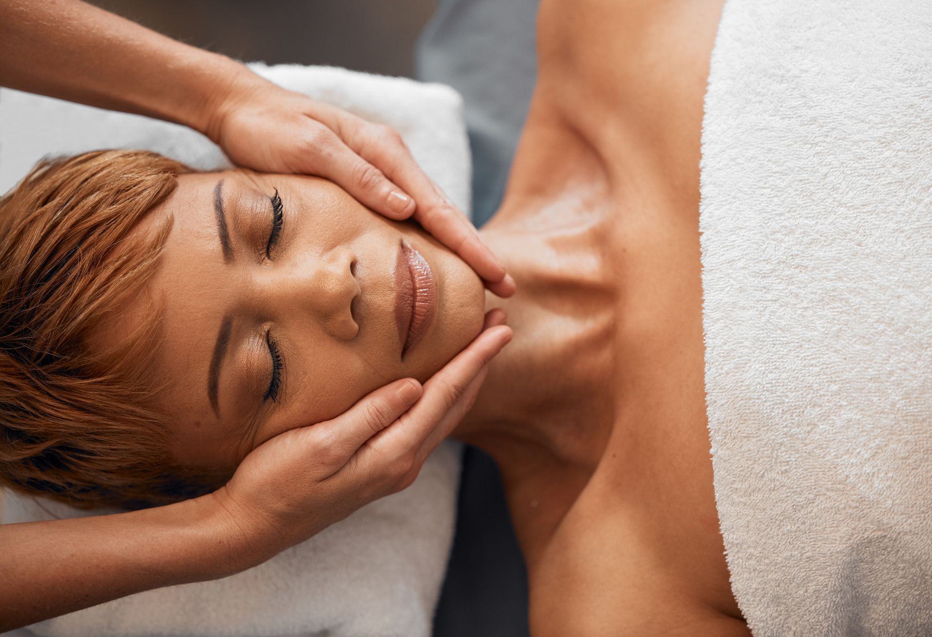 Relaxed person receiving a facial massage on a spa bed, eyes closed, with a white towel nearby