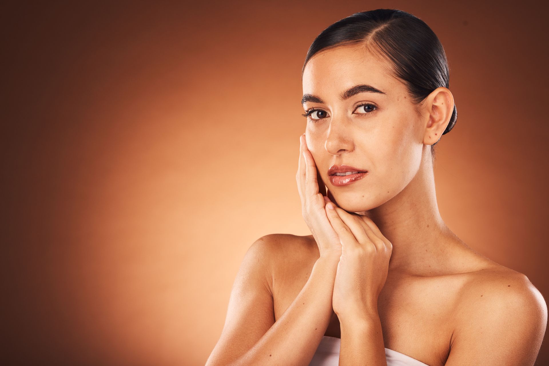 Portrait of a person touching their face against a warm orange background