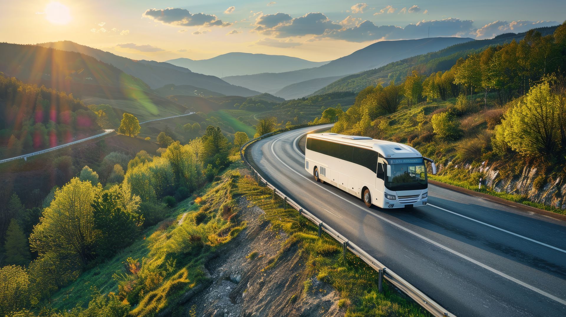 White bus driving on a winding road through a mountain range during sunset.