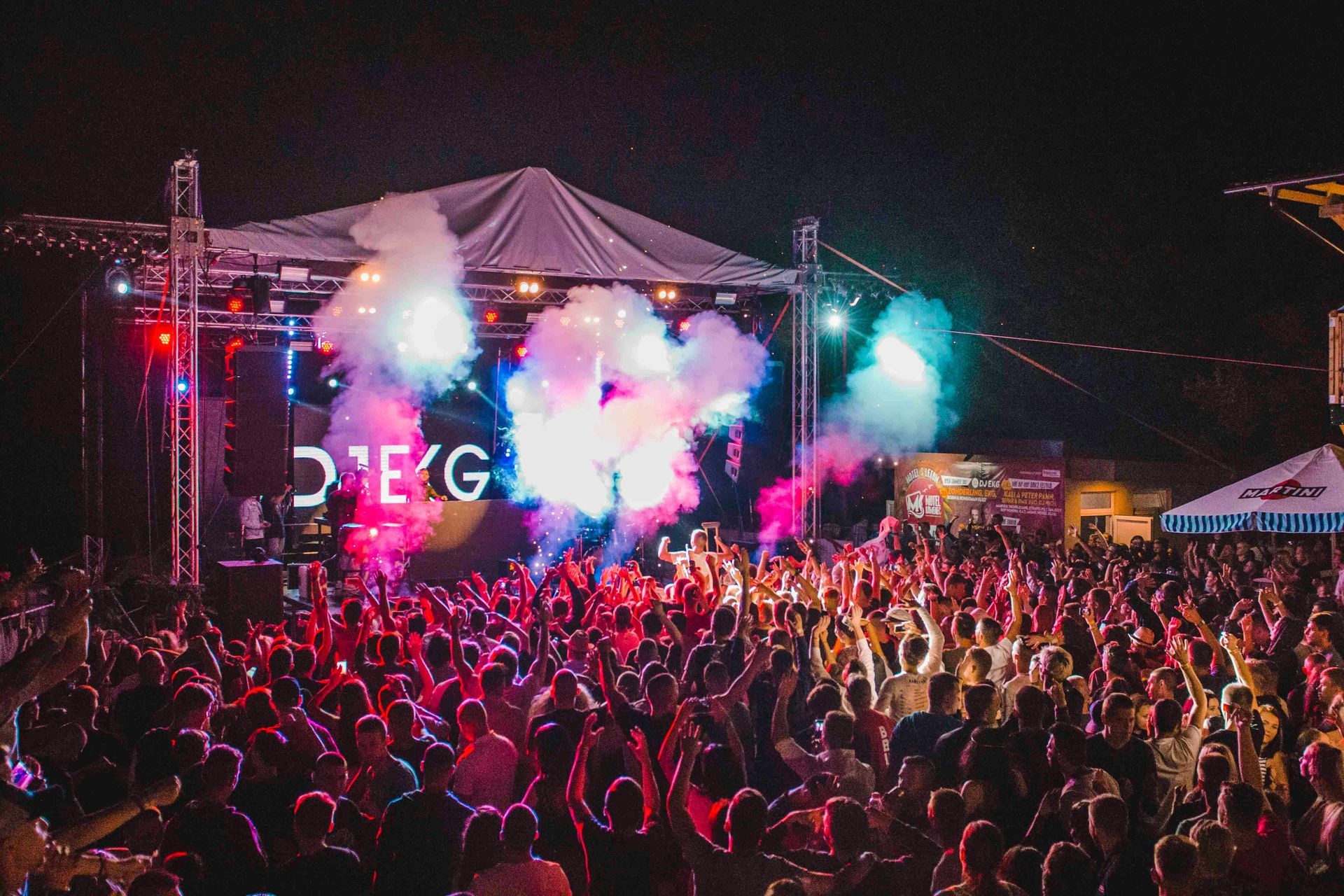 Concert crowd under stage lights and smoke effects; night outdoor setting.