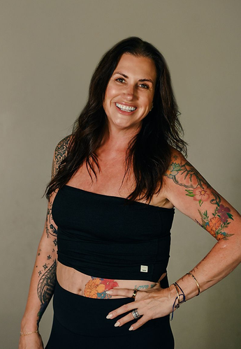 A smiling person wearing a black t-shirt makes a shaka hand gesture against a plain background.