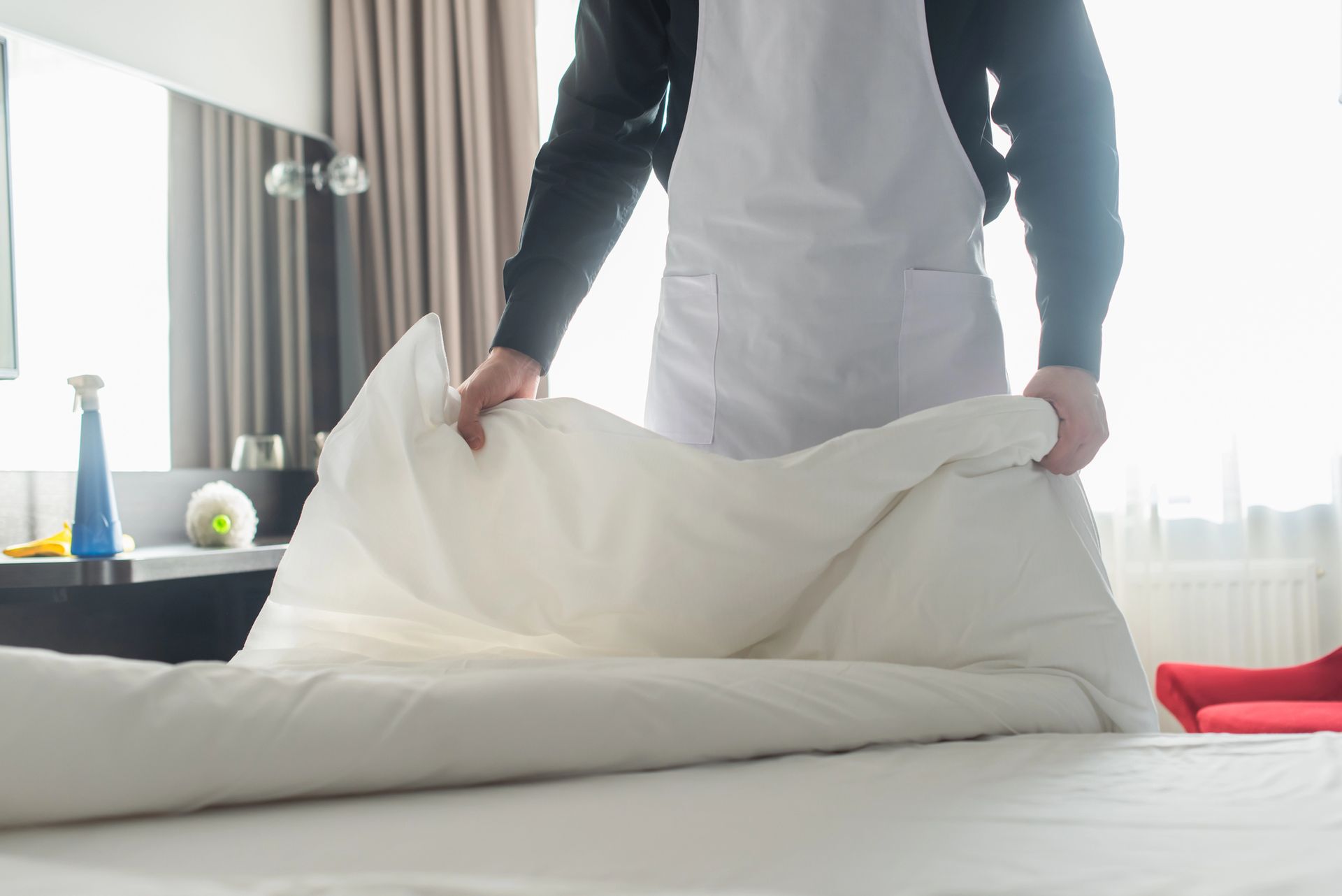 Persona che rifa il letto in una stanza d'albergo, sistemando un piumone bianco.