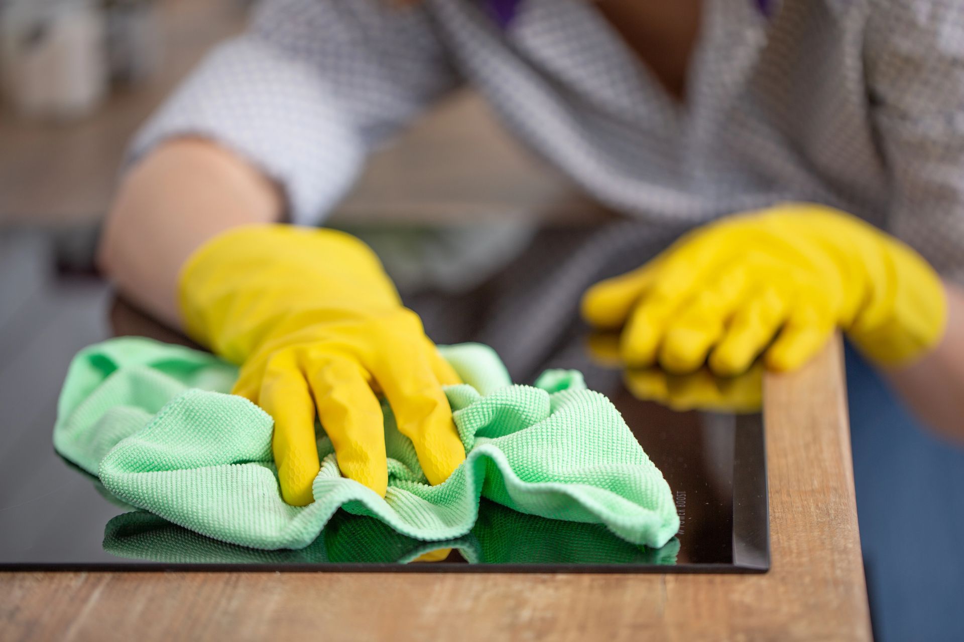 Persona che indossa guanti gialli e pulisce un piano cottura nero con un panno verde.