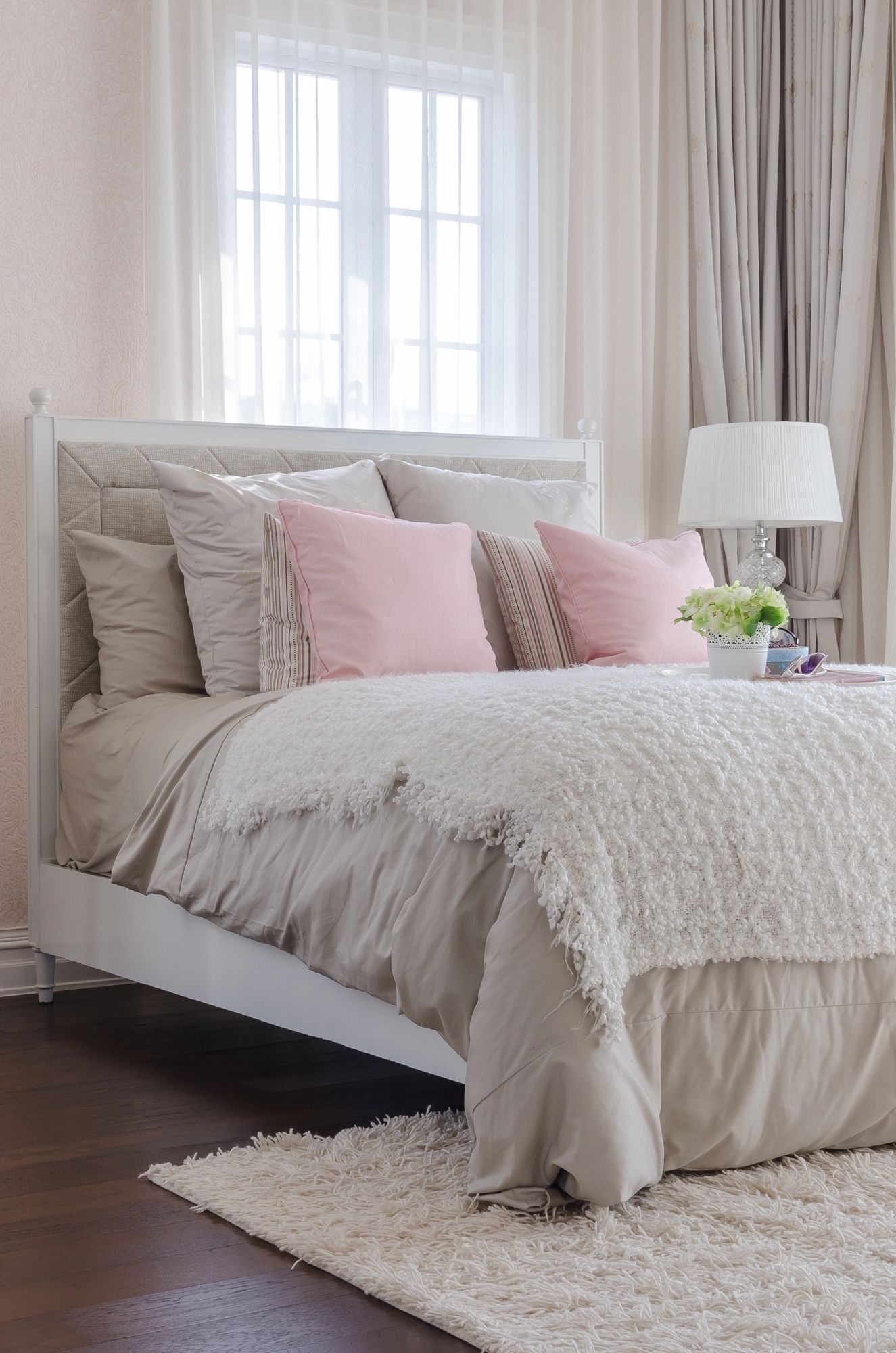 Camera da letto con letto bianco, cuscini rosa e un soffice tappeto bianco.