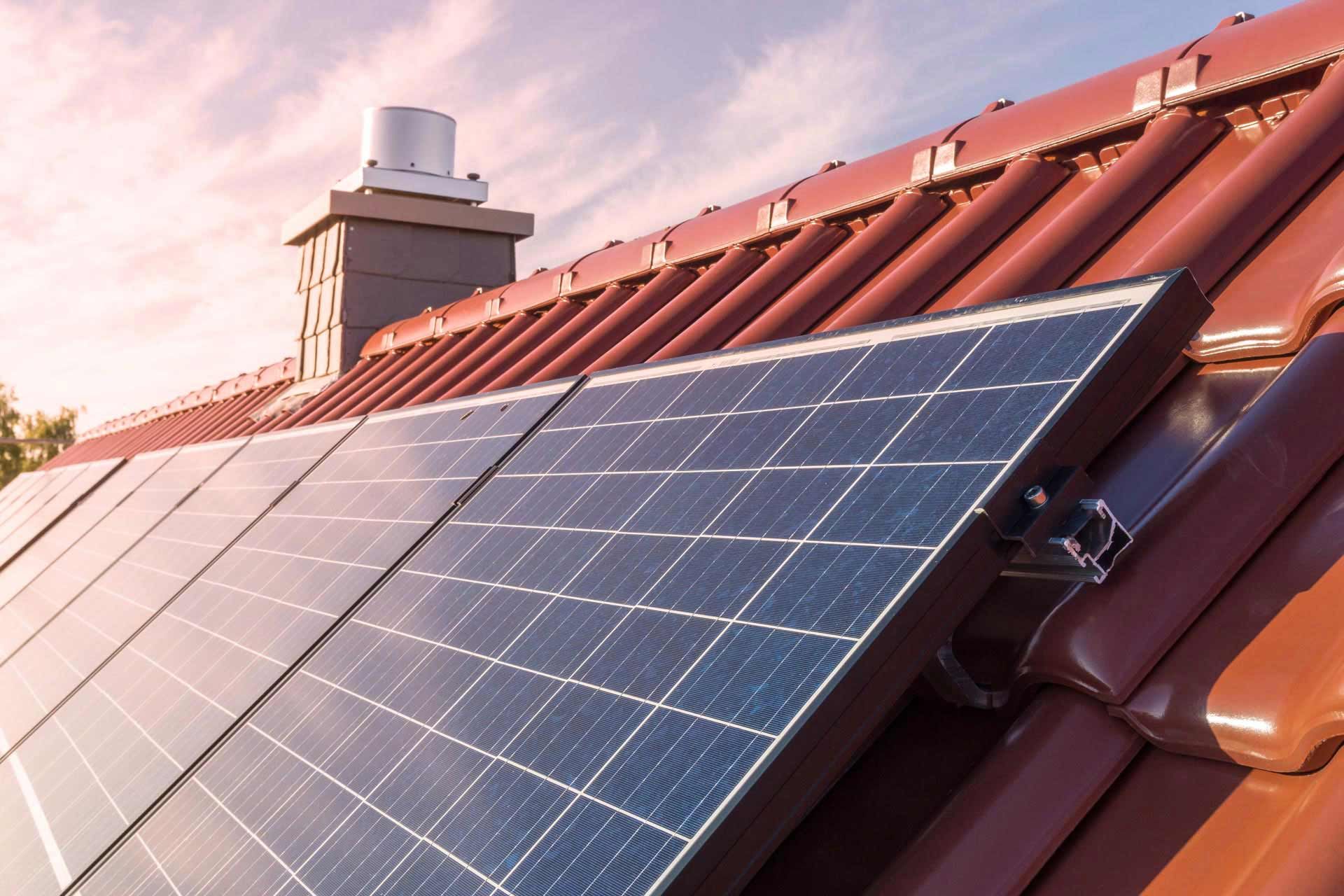 Solar panels on a red-tiled roof under a sky.