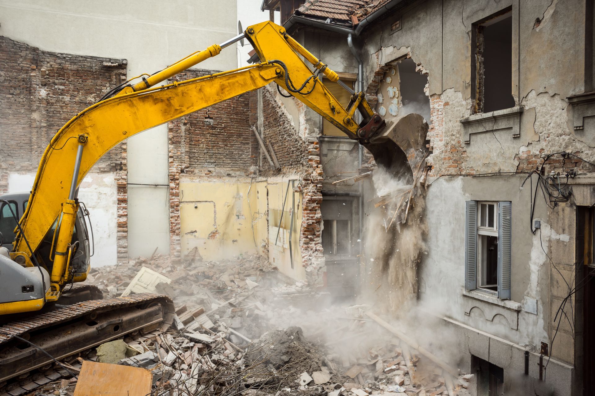 Une excavatrice jaune démolit un bâtiment en briques.