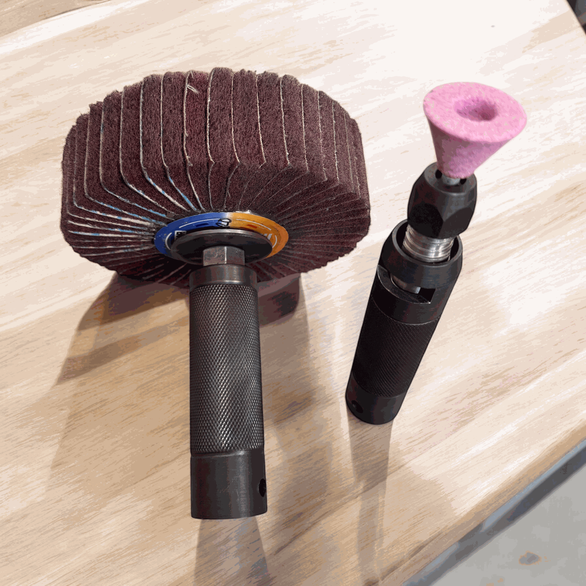 Dos herramientas rotativas manuales con accesorios de lijado sobre un banco de trabajo de madera.