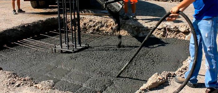 Trabajadores extendiendo hormigón fresco en una obra de construcción con barras de refuerzo y equipo de seguridad naranja.