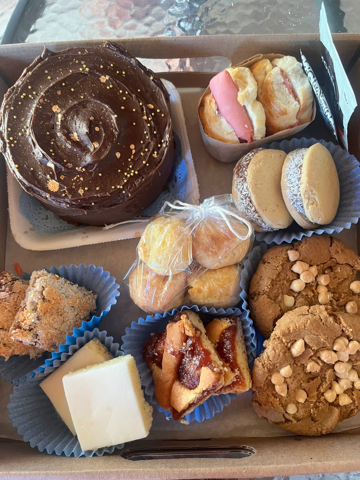 Caja de productos horneados variados, que incluye pastel de chocolate, galletas, sándwiches y pasteles.