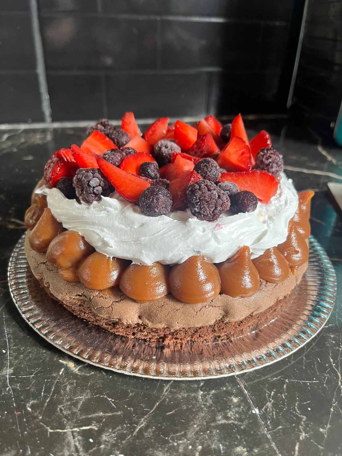 Pastel de chocolate con glaseado de caramelo, crema batida, fresas y moras.