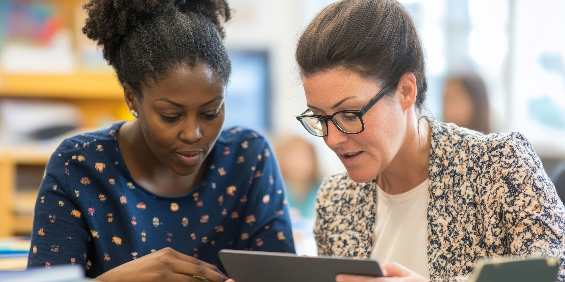 Deux femmes regardant ensemble une tablette, dans une salle de classe.
