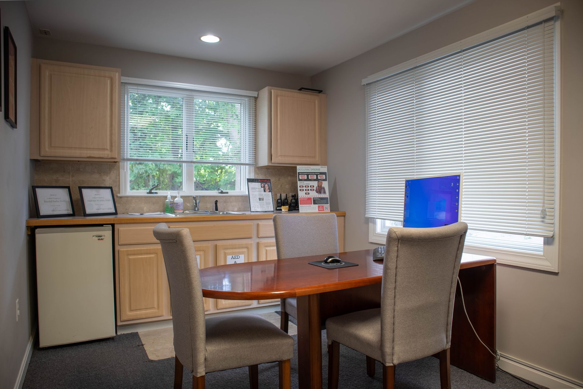 Small kitchen nook with dining table, two chairs, cabinets, window, and a laptop on the desk