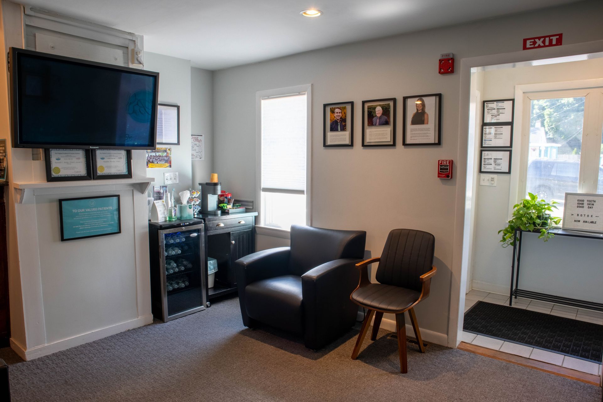 Waiting room with TV, chairs, framed art, and an exit door near a window.