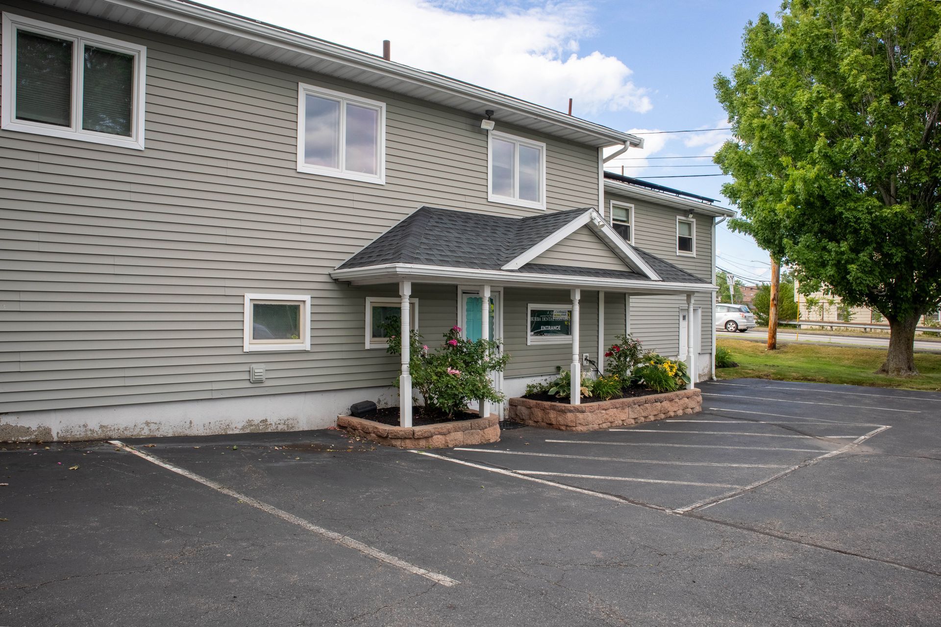 Gray apartment building entrance with white trim, small porch, and empty parking lot