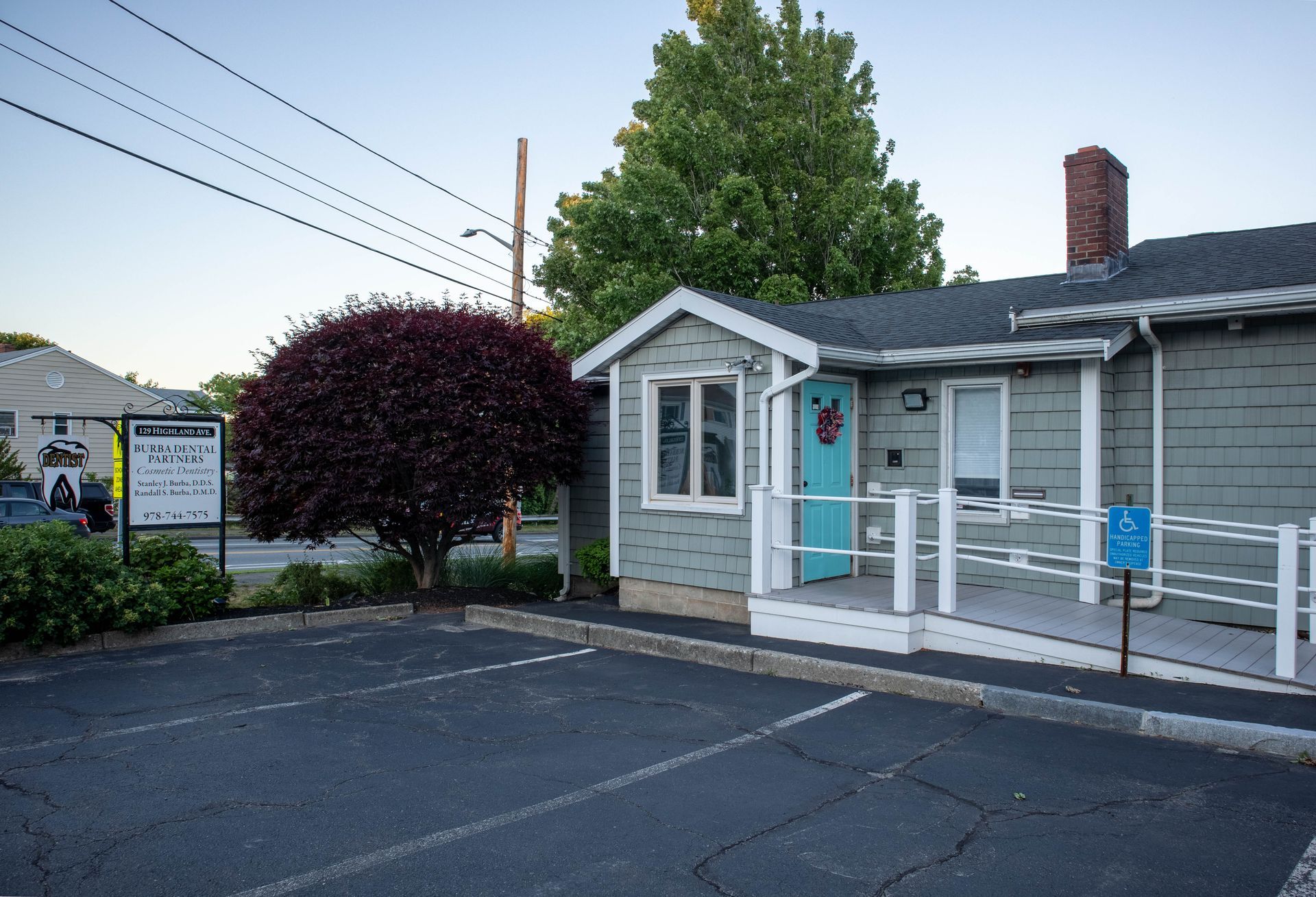 Small gray building with blue door and ramp, beside an empty parking lot at dusk.
