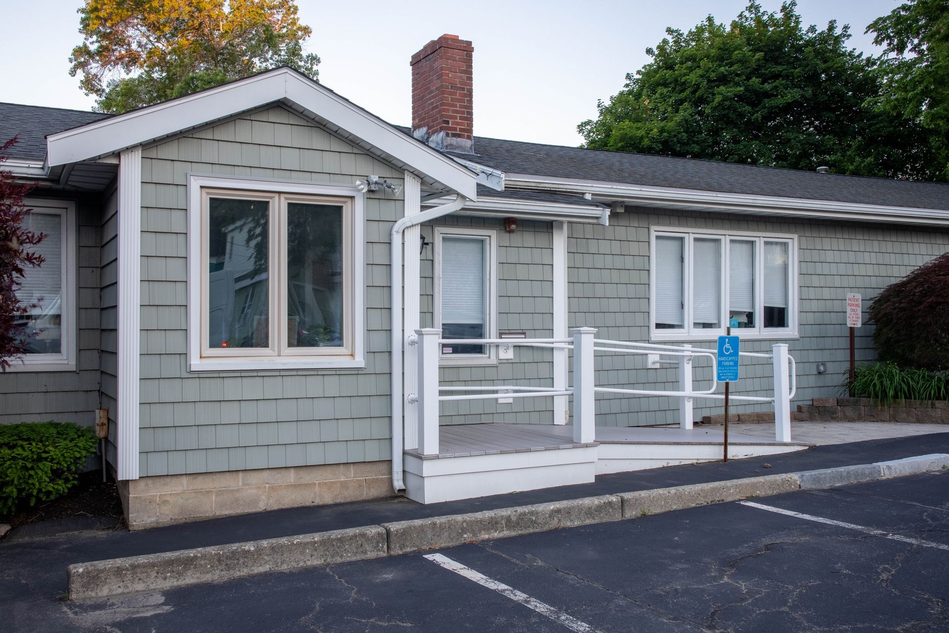 Small gray building with a white porch, ramp, and blue accessibility sign