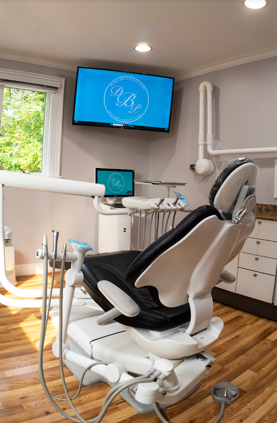 Dental treatment room with a reclining chair, monitors, and white cabinets in a modern clinic