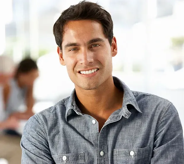 Smiling man in a gray shirt seated indoors with a blurred office background