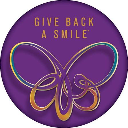 Purple circular logo with gold butterfly and “GIVE BACK A SMILE” text