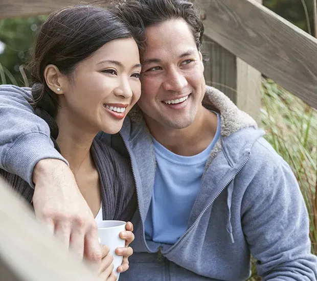 Smiling couple sitting outdoors on wooden steps, leaning close and holding a cup