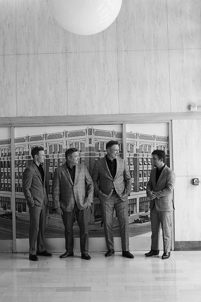 Four men stand outside a glass storefront in a black-and-white photo.