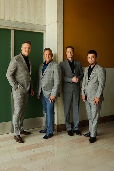 Four men in gray suits standing together in a hallway, posing for a photo.