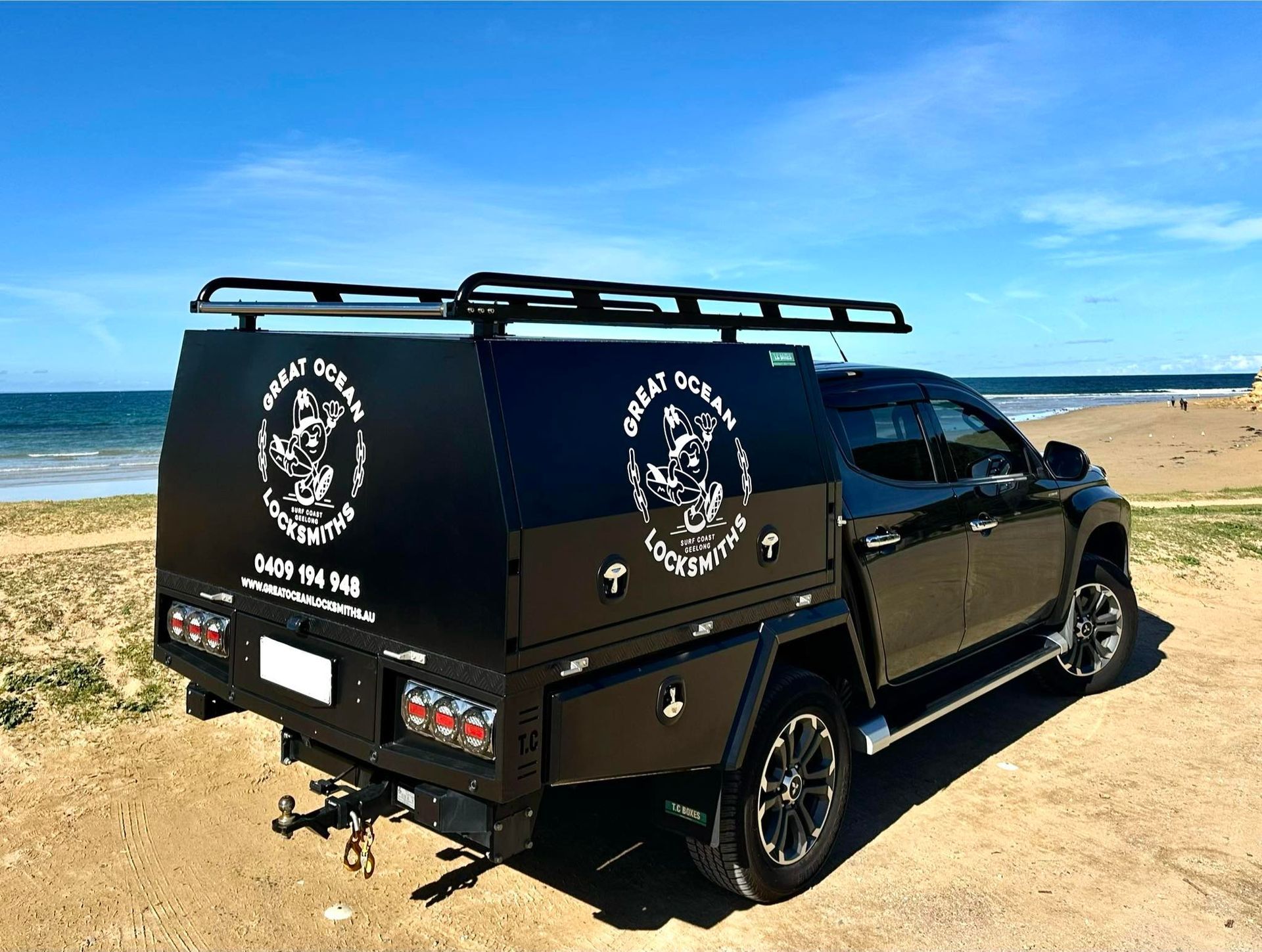 Black pickup truck with custom canopy parked on a beach, logo on sides, blue sky — Great Ocean Locksmiths in Belmont, VIC