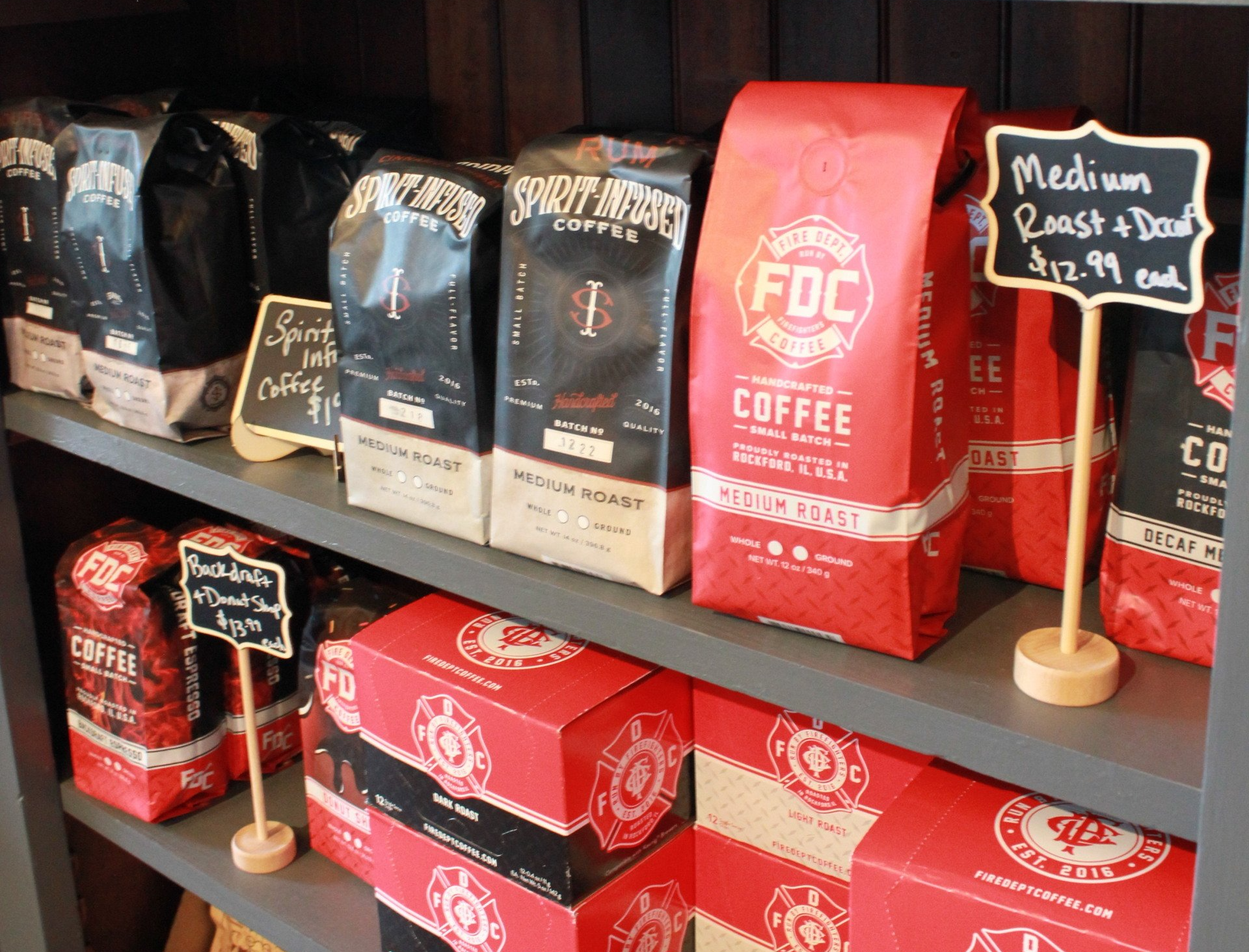 Coffee bags and boxes on a shelf. Red and black packaging with small chalkboard signs.
