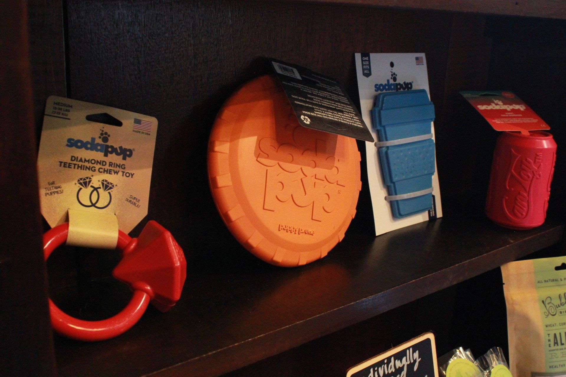 Dog toys in a retail display: red ring, orange frisbee, blue bands, and a pink can.