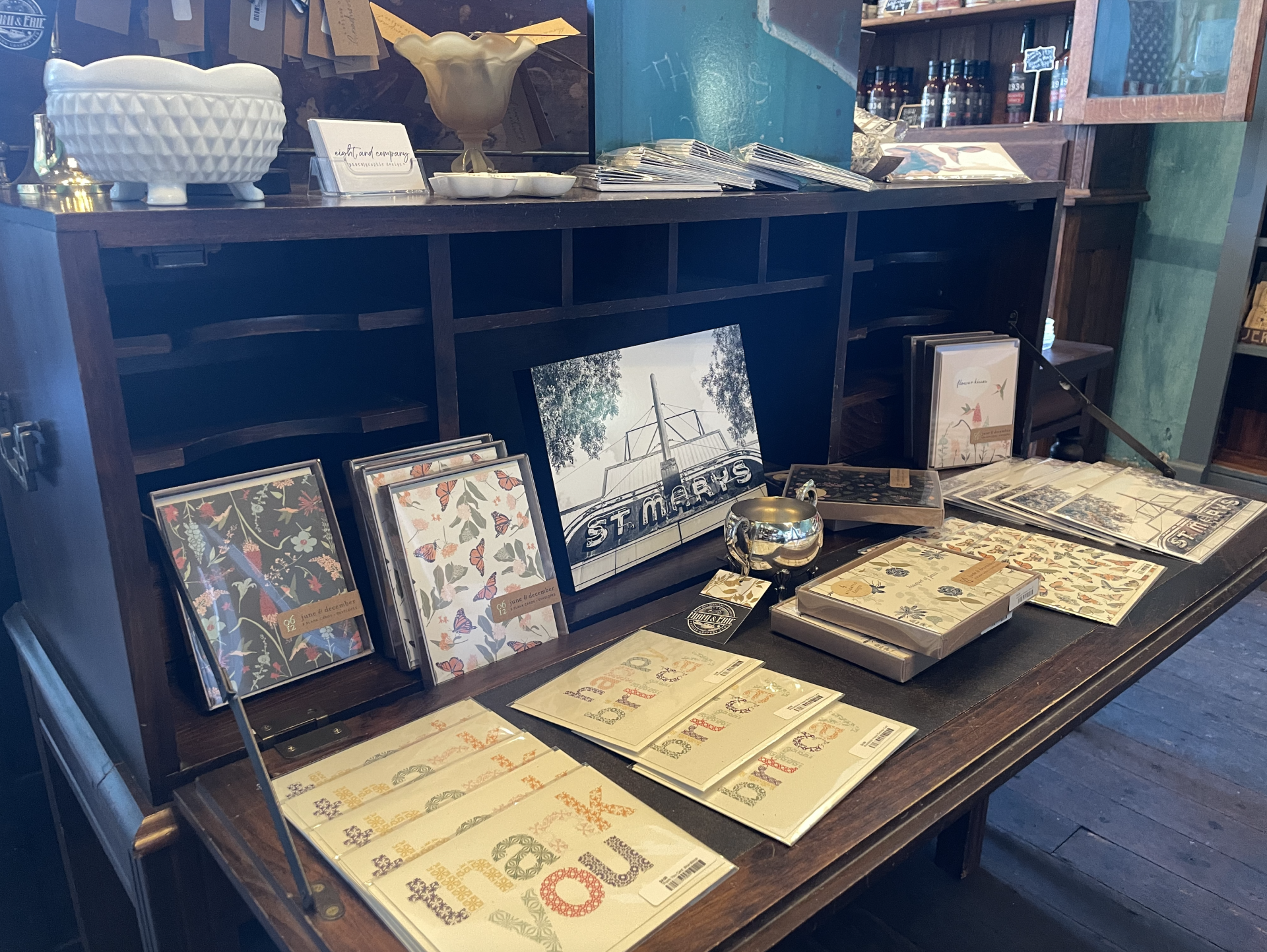 A wooden desk displays stationery: cards, journals, and a small gold bird figurine.