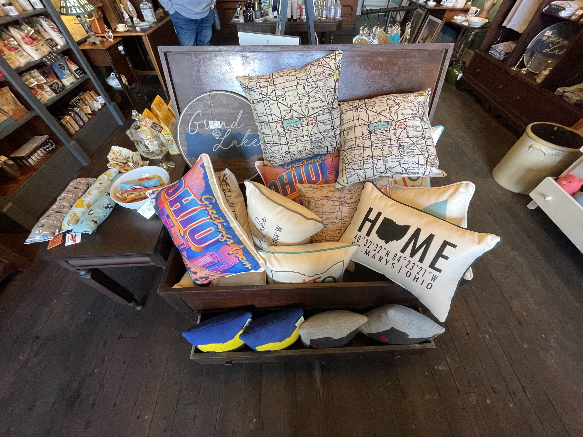 Display of decorative pillows in a shop, various colors and patterns. Shelf with more pillows.