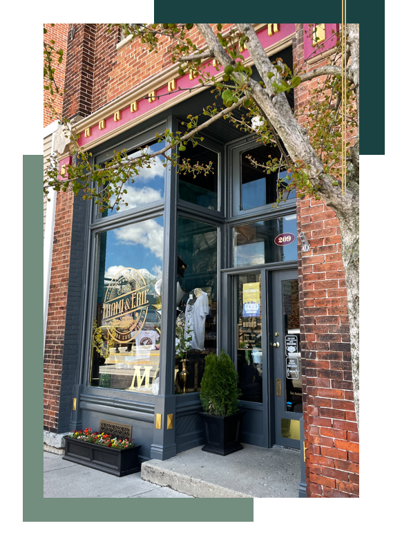 Exterior of a storefront with large windows; red brick building with dark gray trim; small tree on right.