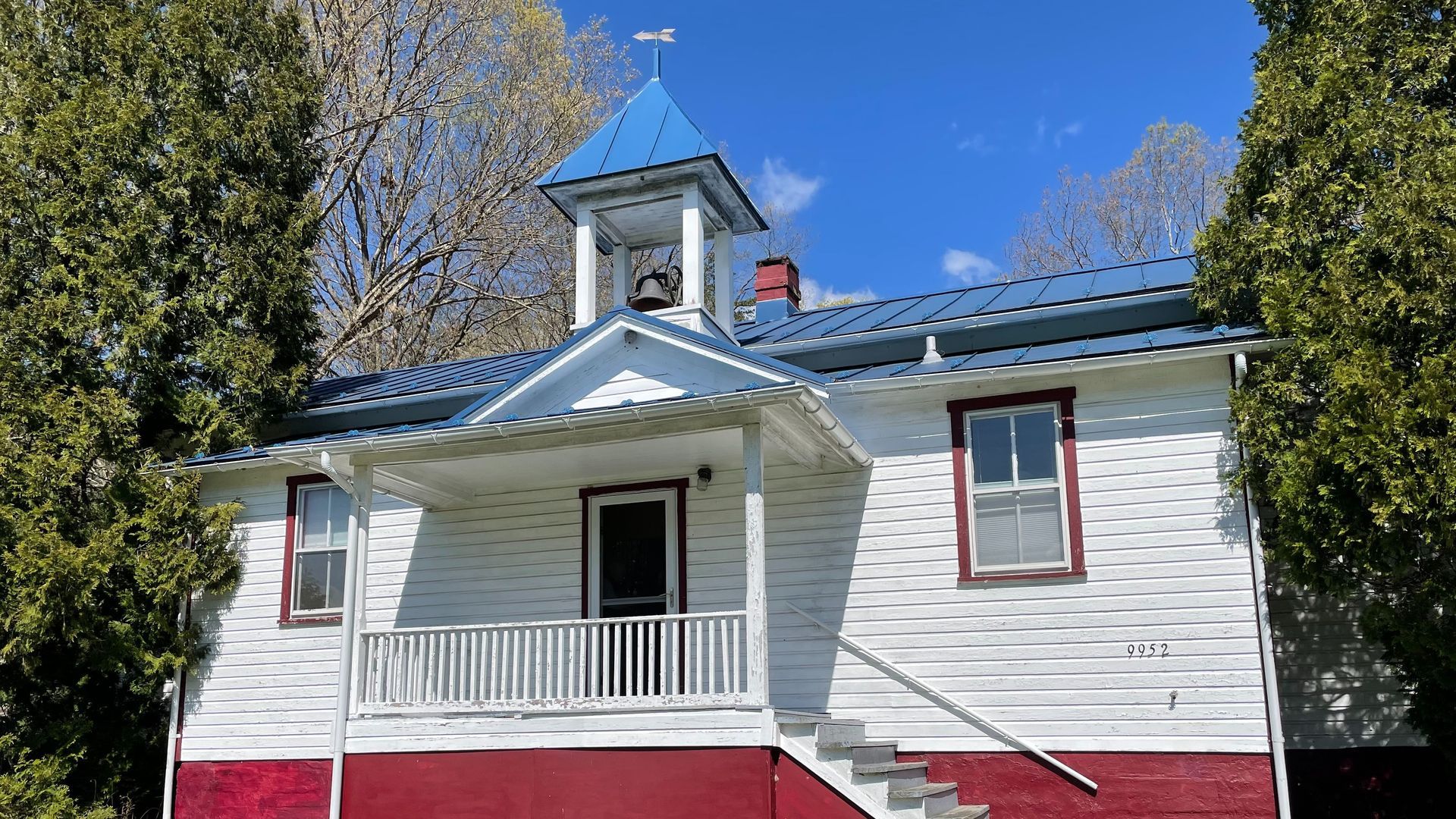 A white and red house with a blue roof and a bell tower.
