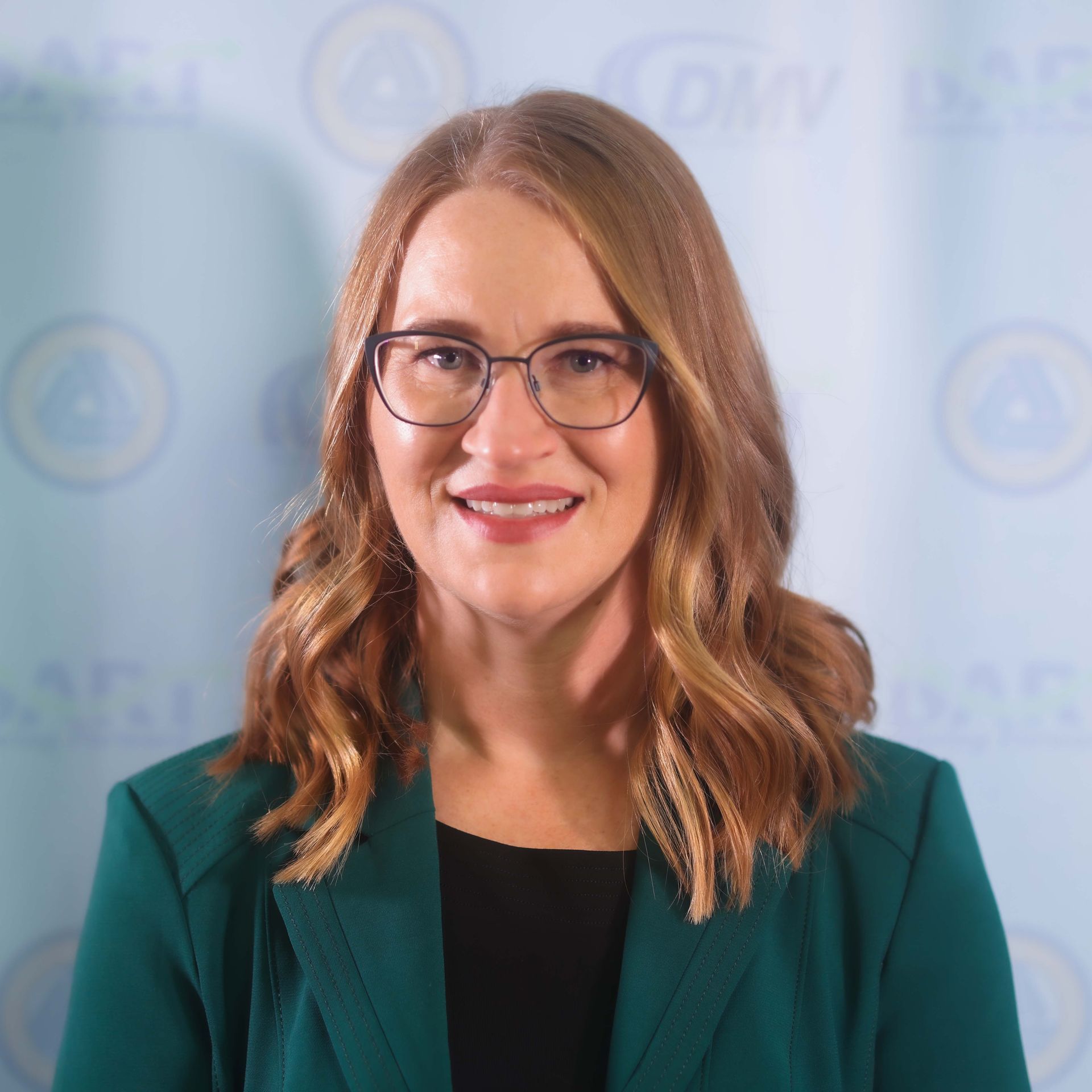 A woman wearing glasses and a green jacket smiles for the camera